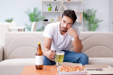 Pizza yiyen adam evde yemek yiyor, dinleniyor.