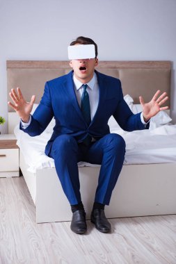 Yatak odasında sanal gerçeklik kulaklığı takan bir iş adamı.