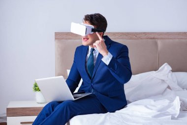 Yatak odasında sanal gerçeklik kulaklığı takan bir iş adamı.