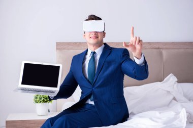 Yatak odasında sanal gerçeklik kulaklığı takan bir iş adamı.