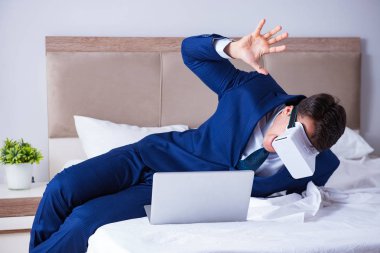 Yatak odasında sanal gerçeklik kulaklığı takan bir iş adamı.