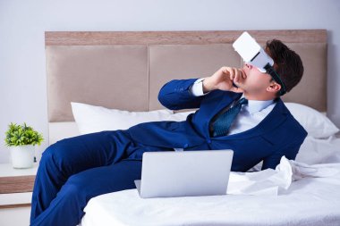 Yatak odasında sanal gerçeklik kulaklığı takan bir iş adamı.