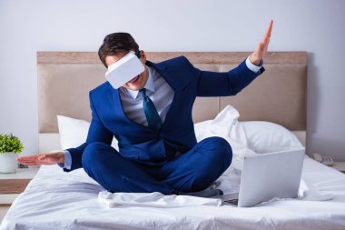 Yatak odasında sanal gerçeklik kulaklığı takan bir iş adamı.