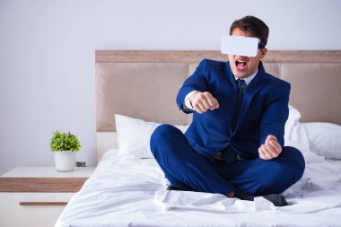 Yatak odasında sanal gerçeklik kulaklığı takan bir iş adamı.