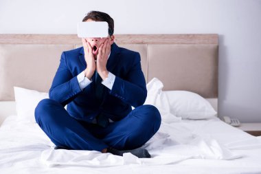 Yatak odasında sanal gerçeklik kulaklığı takan bir iş adamı.