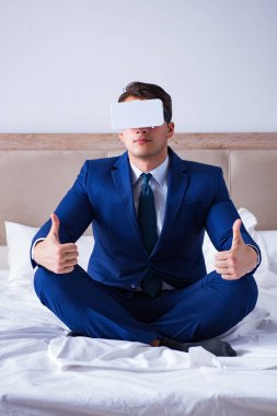 Yatak odasında sanal gerçeklik kulaklığı takan bir iş adamı.