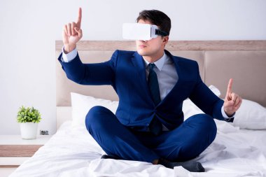 Yatak odasında sanal gerçeklik kulaklığı takan bir iş adamı.
