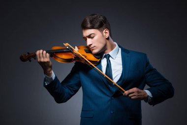 Genç adam karanlık odada keman çalıyor.