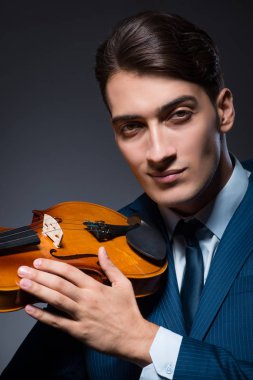 Genç adam karanlık odada keman çalıyor.