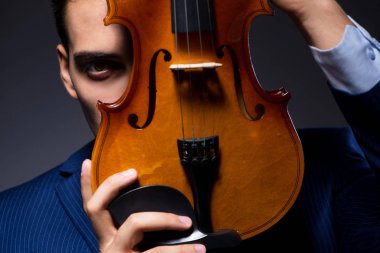 Genç adam karanlık odada keman çalıyor.