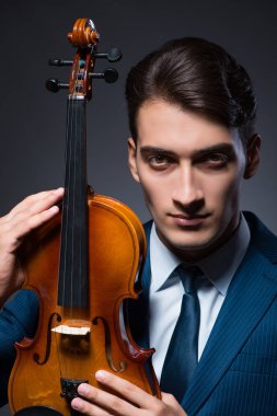 Genç adam karanlık odada keman çalıyor.