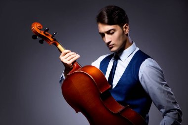 Genç adam karanlık odada çello çalıyor.