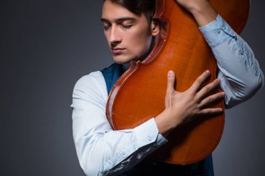 Genç adam karanlık odada çello çalıyor.