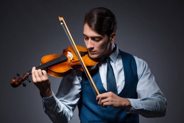 Genç adam karanlık odada keman çalıyor.