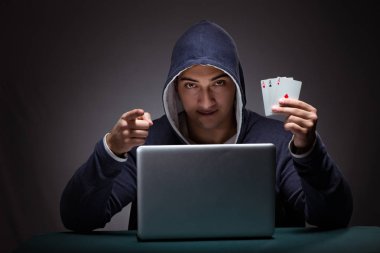 Kapüşonlu genç adam dizüstü bilgisayarın önünde oturuyor.