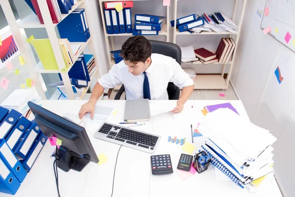 Geschäftsmann arbeitet im Büro mit Stapeln von Büchern und Papieren — Stockfoto