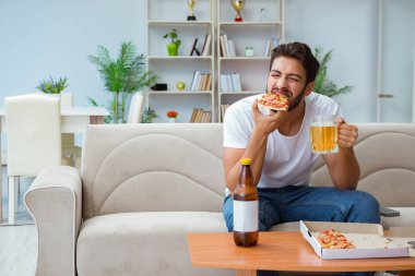 Pizza yiyen adam evde yemek yiyor, dinleniyor.