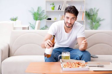 Pizza yiyen adam evde yemek yiyor, dinleniyor.