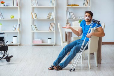Genç adam ameliyattan sonra koltuk değnekleriyle evde iyileşiyor.