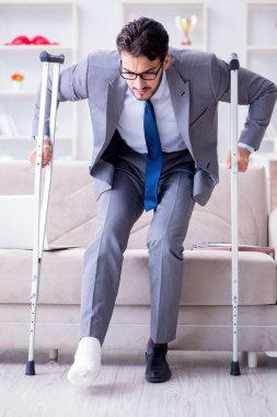 Koltuk değneği ve kırık bacağı olan bir iş adamı.