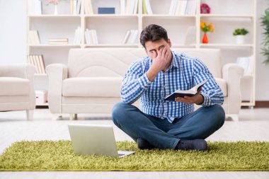 Genç yakışıklı adam evde yerde oturuyor.