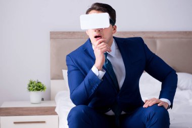 Yatak odasında sanal gerçeklik kulaklığı takan bir iş adamı.