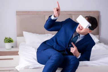 Yatak odasında sanal gerçeklik kulaklığı takan bir iş adamı.