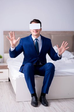 Yatak odasında sanal gerçeklik kulaklığı takan bir iş adamı.