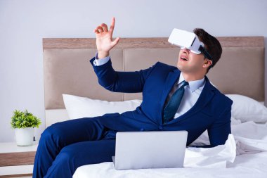 Yatak odasında sanal gerçeklik kulaklığı takan bir iş adamı.