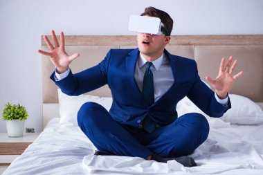 Yatak odasında sanal gerçeklik kulaklığı takan bir iş adamı.