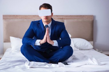 Yatak odasında sanal gerçeklik kulaklığı takan bir iş adamı.
