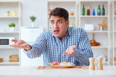 Genç koca öğle yemeğinde tatsız yemekler yiyor.