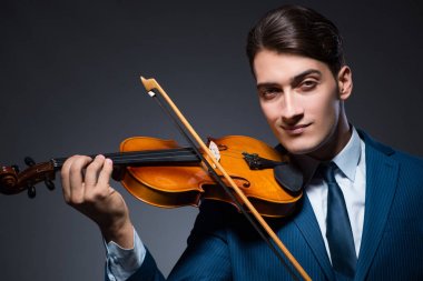 Genç adam karanlık odada keman çalıyor.