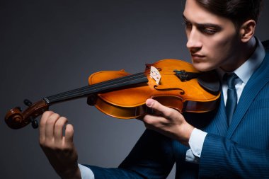 Genç adam karanlık odada keman çalıyor.