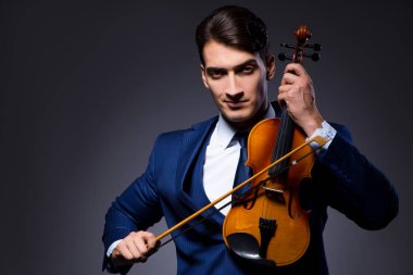 Genç adam karanlık odada keman çalıyor.