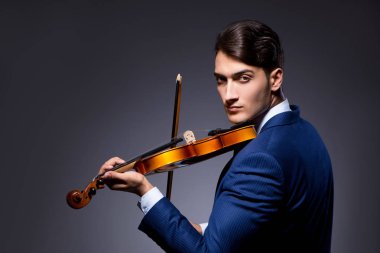 Genç adam karanlık odada keman çalıyor.