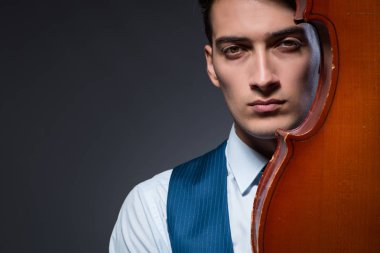 Genç adam karanlık odada çello çalıyor.