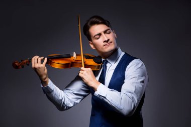 Genç adam karanlık odada keman çalıyor.