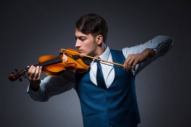 Genç adam karanlık odada keman çalıyor.