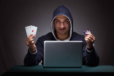 Kapüşonlu genç adam dizüstü bilgisayarın önünde oturuyor.