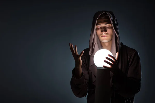 Jovem feiticeiro com bola de cristal no quarto escuro — Fotografia de Stock