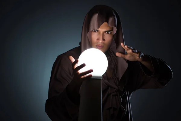 Молодий чарівник з кришталевим м'ячем у темній кімнаті — стокове фото