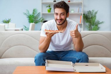 Pizza yiyen adam evde yemek yiyor, dinleniyor.