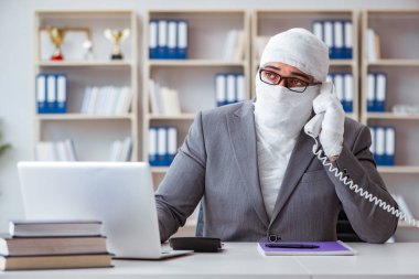 Bandajlı işadamı büroda kağıt işleriyle uğraşıyor.