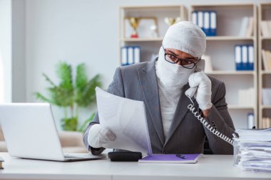 Bandajlı işadamı büroda kağıt işleriyle uğraşıyor.