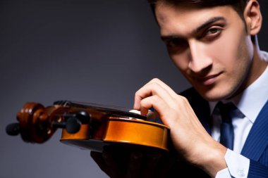 Genç adam karanlık odada keman çalıyor.