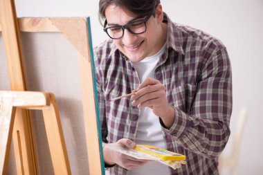 Genç erkek sanatçı parlak stüdyoda resimler çiziyor.