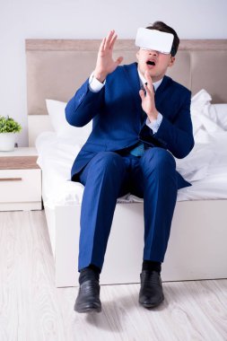 Yatak odasında sanal gerçeklik kulaklığı takan bir iş adamı.
