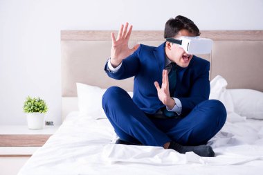Yatak odasında sanal gerçeklik kulaklığı takan bir iş adamı.