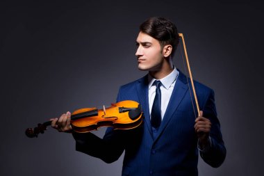 Genç adam karanlık odada keman çalıyor.